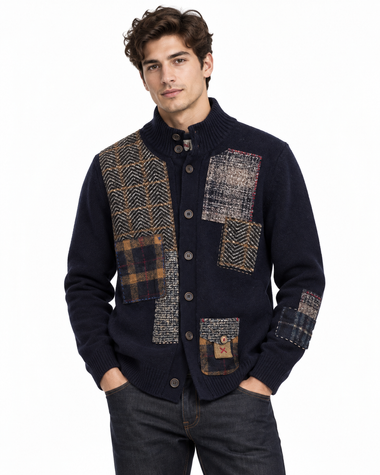 A man wearing a navy blue knit cardigan with large patchwork wool panels in herringbone and plaid patterns, paired with dark jeans against a plain white background.