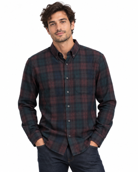 A man wearing a long-sleeve button-down plaid shirt in dark red and navy blue, paired with dark jeans, against a plain white background.