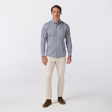 A man modeling a blue and white checkered long-sleeve button-down shirt, paired with beige pants and brown shoes, standing against a light gray studio background.