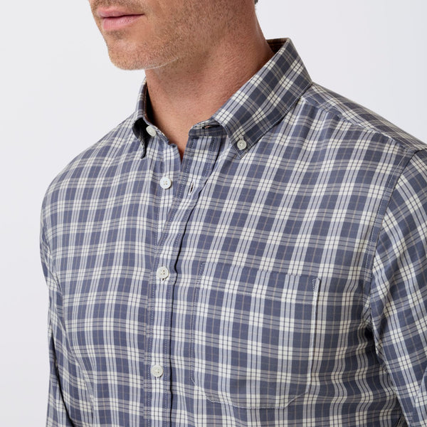 A close-up of a man wearing a blue and white plaid button-down shirt, showing the collar, buttons, and chest area against a plain light background.